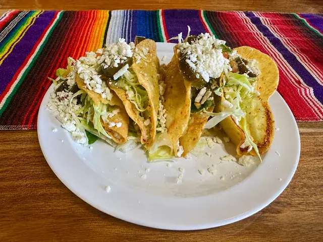 Three crispy tacos topped with lettuce, cheese, and jalapeño at Nina's Tacos