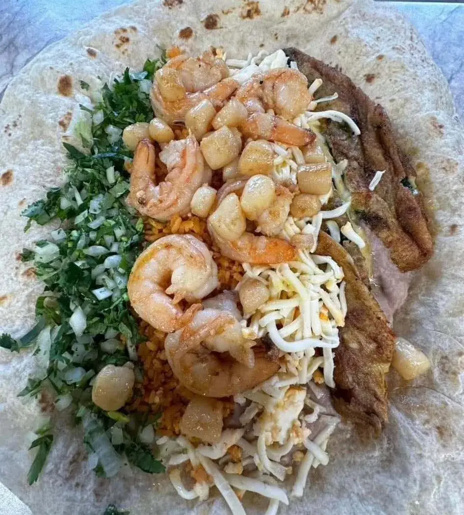 Shrimp, rice, and herbs on an open tortilla during preparation at Nina's Tacos